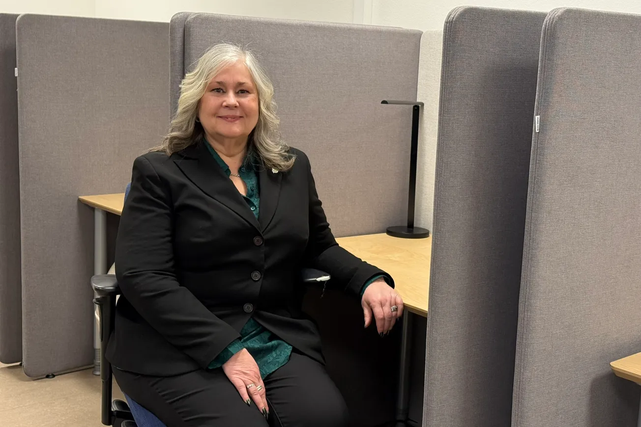 Christine som är utbildningsledare på Yrkeshögskolan Mitt sitter vid en dator med gråa skärmväggar.
