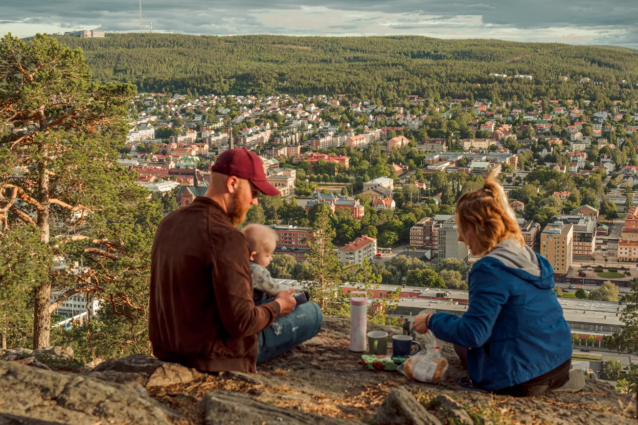 En man och en kvinna sitter på toppen av Norra Berget och har picknick. Mannen har ett barn i knät.