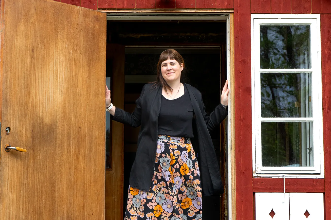 En kvinna som står i dörröppningen till ett rött hus.