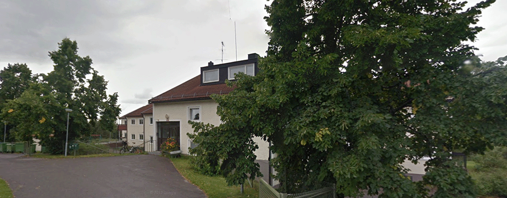 En gata med ett hus och träd i bakgrunden.