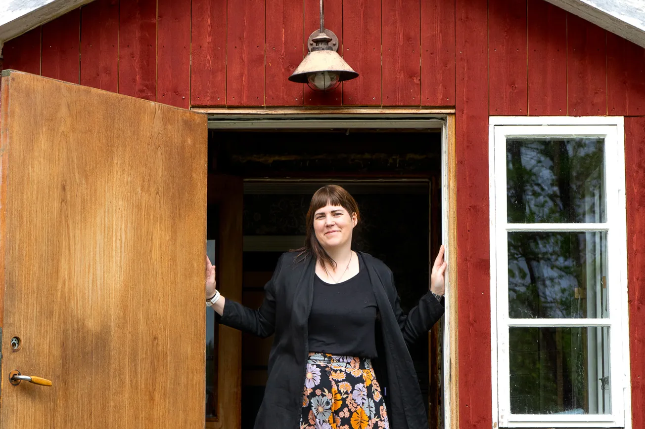 En kvinna som står i dörröppningen till ett rött hus.