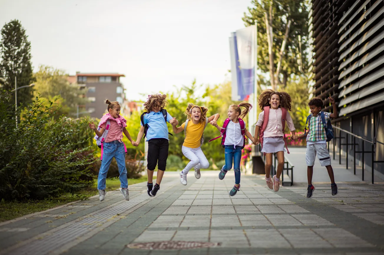 En grupp glada grundskolebarn gör ett gemensamt hopp på skolgården.