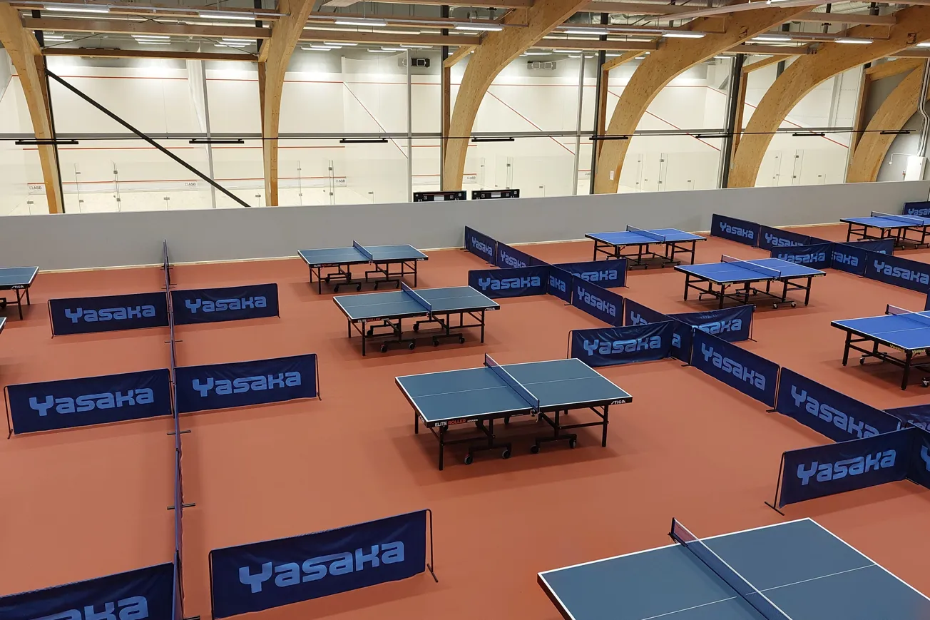 Idrottshall med flera bordtennisbord uppställda.