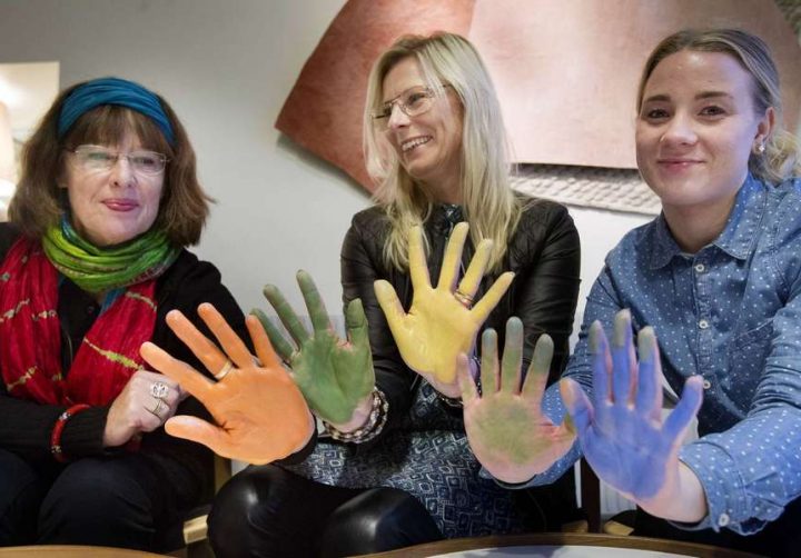 Tre personer håller upp sina händer mot kameran, händerna är täckta av färg i olika färger.