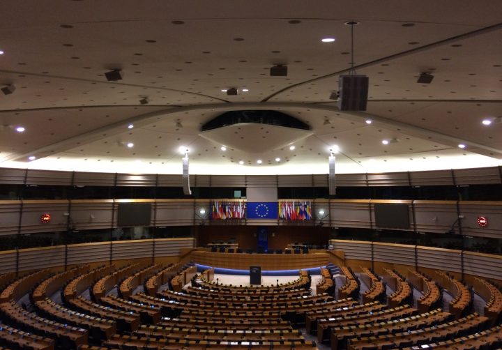 En väldigt stor sal med sittplatser för många, EU flaggan och många flaggor finns uppradade längst fram.
